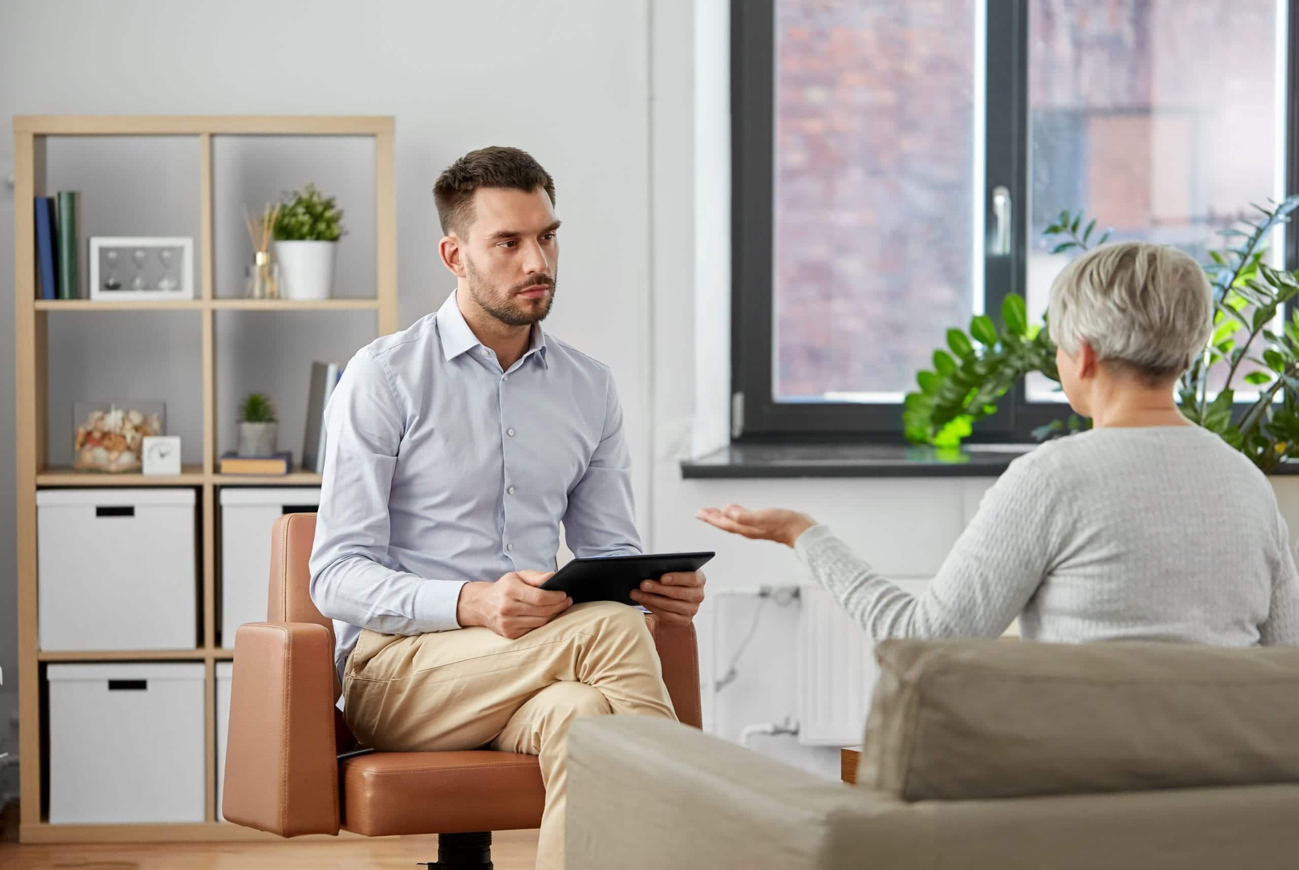 young man seated in office setting taking notes while colleague explains something