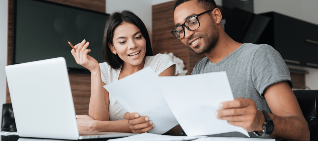 man and woman looking at documents while working on a laptop