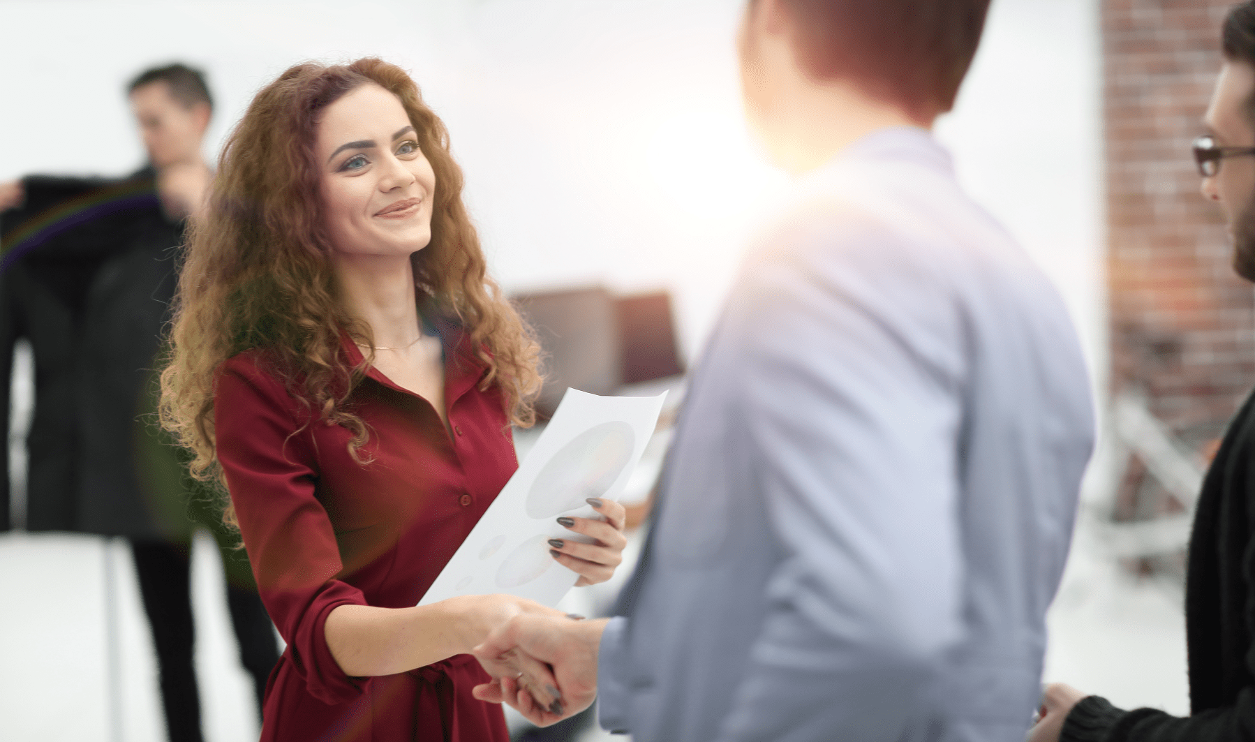 young woman holding business documents while shaking a man's hand