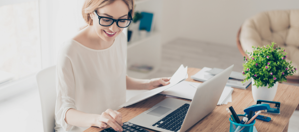 woman working at laptop in bright office with important documents and a calculator in front of her