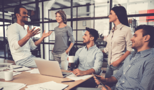 five men and women casually gathered around a table discussing business strategy