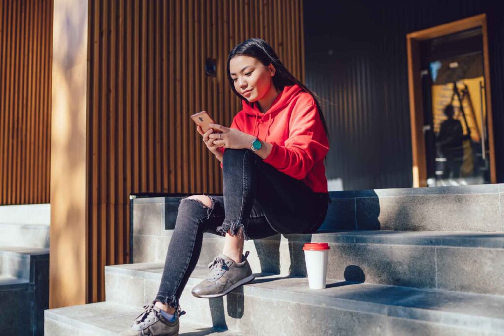 teenage girl sitting on step using a mobile app on her phone