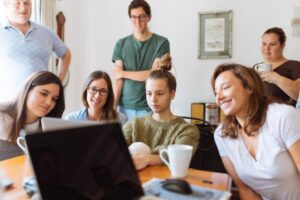 room full of men and women gathered around a laptop engaged in team building