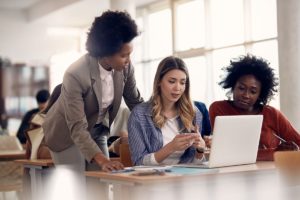 woman sitting at laptop with two other people explaining the difference between medical billing vs revenue cycle management