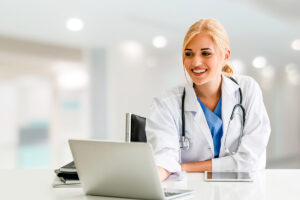 a doctor smiles as they look on a computer, realizing the benefits of a medical records audit